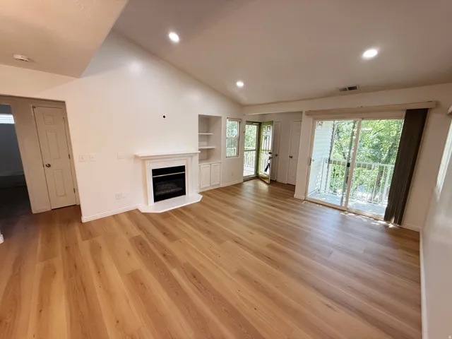 Vaulted ceiling, wood-finish flooring, built-in shelving, fireplace, and sliding glass door to exterior balcony