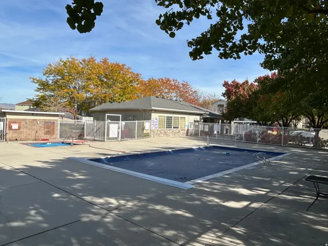 Community pool area featuring two covered pools, a stone-accented clubhouse, and perimeter fencing