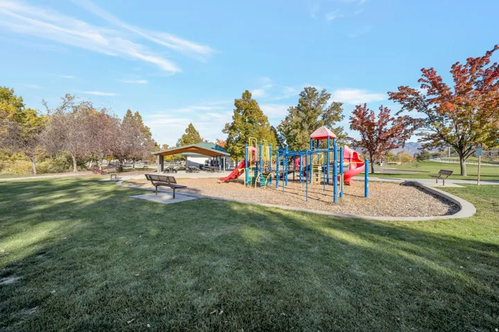 Expansive park area featuring a colorful playground, a covered picnic pavilion, and mature trees with autumn foliage