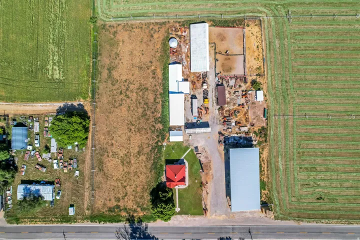 Aerial perspective showcasing an expansive property featuring multiple outbuildings, a red-roofed residence, and a paved road frontage
