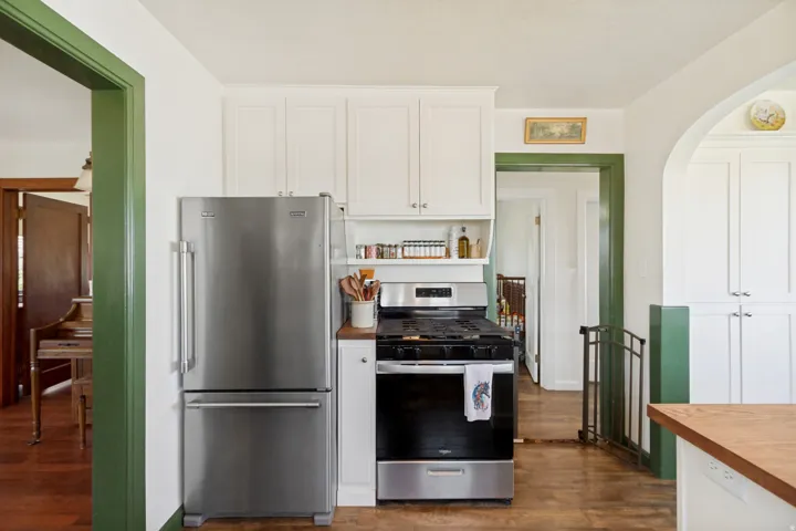 Kitchen featuring stainless steel refrigerator and range, white upper cabinetry, wood-finish flooring, and a wood countertop