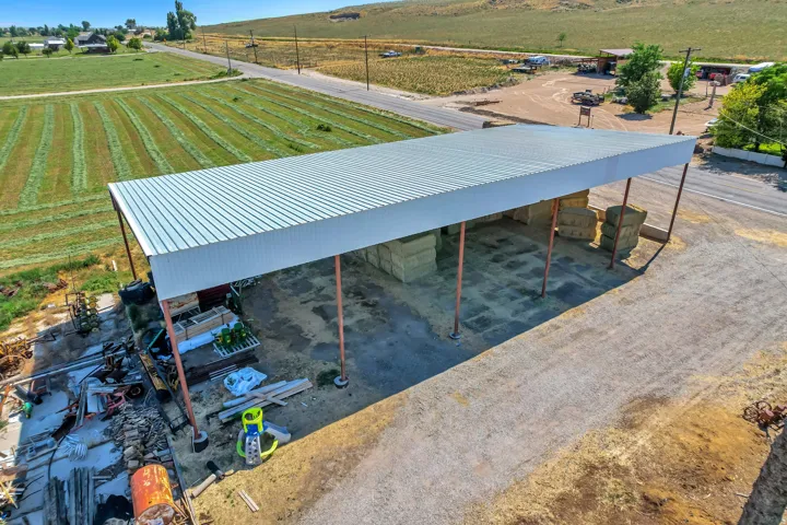 Expansive open-air metal roof structure with support columns, adjacent to a large unpaved area