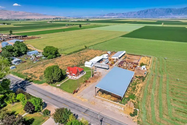 Expansive agricultural property featuring a red-roofed residence, multiple outbuildings, and a large metal-roofed barn structure