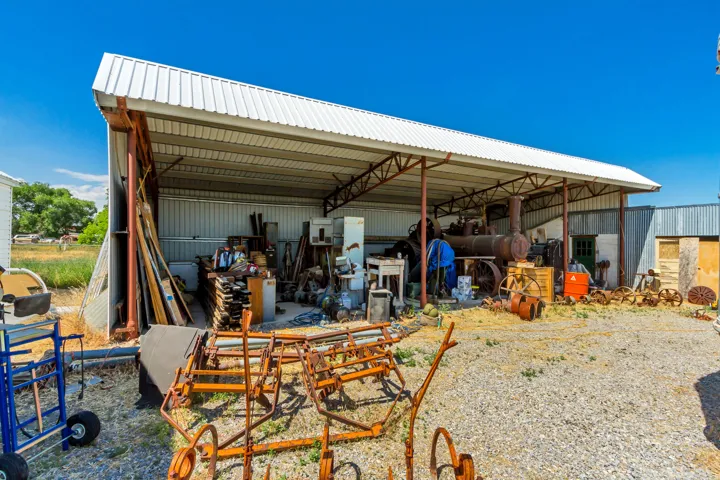 Open-sided metal shed featuring a corrugated roof and a gravel floor.