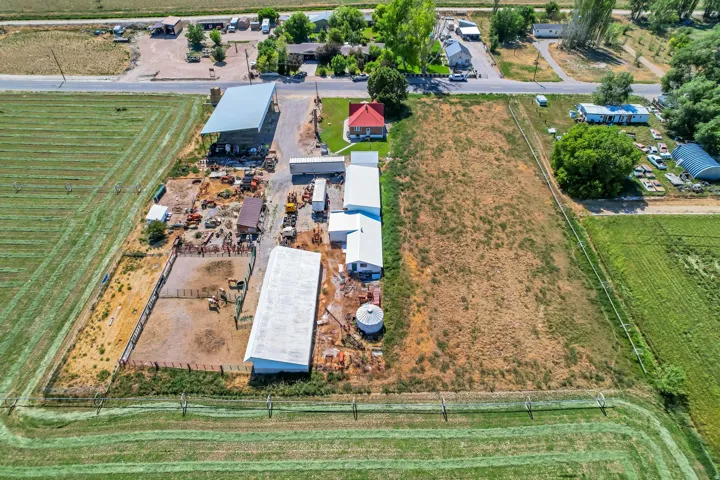 Expansive property featuring a red-roofed residence, multiple large outbuildings, fenced enclosures, and a significant undeveloped land area