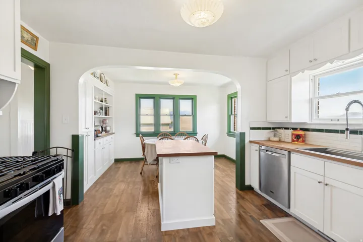 Bright kitchen featuring white cabinetry, wood-finish flooring, and a stainless steel dishwasher