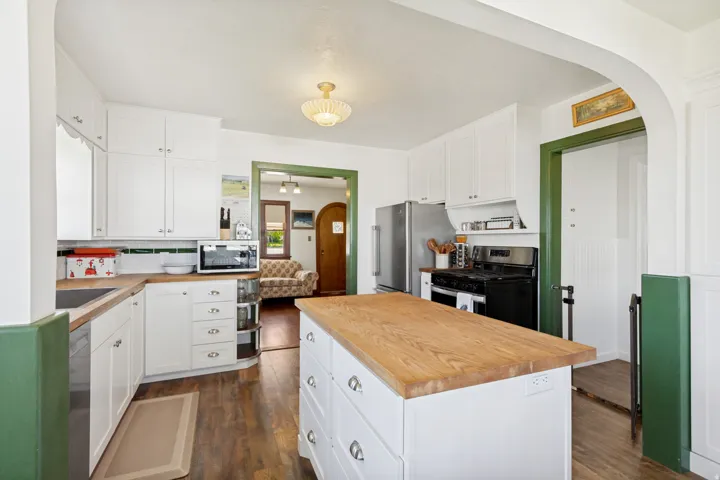 Kitchen featuring a large central island with a wood-finish countertop, white cabinetry, integrated stainless-steel refrigerator, and a gas range