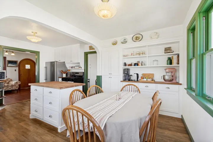 Dining area featuring wood-finish flooring, white built-in cabinetry, an arched entry, and green trim accents