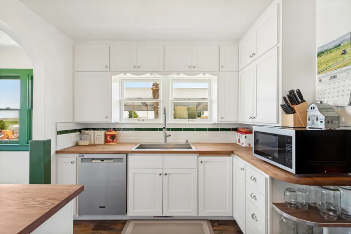 Kitchen featuring white cabinetry, wood-finish countertops, subway tile backsplash with accent trim, stainless steel dishwasher, and an arched doorway