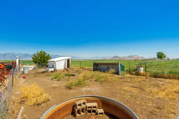 Expansive outdoor space featuring a white slatted utility shed, green pastures, mountain scenery, and a galvanized metal water trough
