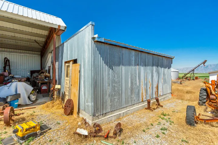 Corrugated metal outbuilding with a concrete foundation, featuring a wood door and an attached covered structure