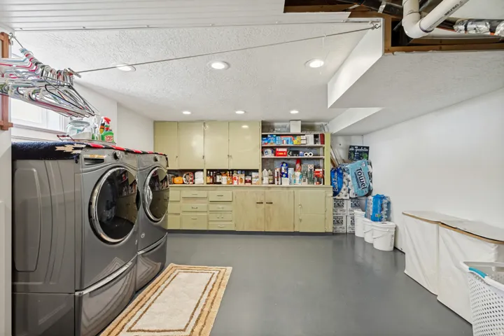 Dedicated laundry area featuring a full-size washer and dryer, extensive built-in cabinetry, recessed ceiling lighting, and a window for natural light
