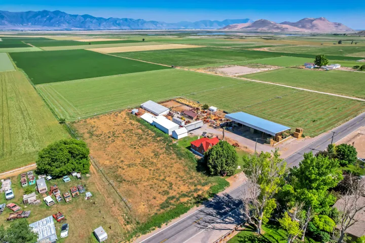 Expansive rural property featuring an enclosed red-roofed structure, multiple white auxiliary buildings, and a large open-sided shelter