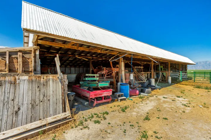 Open-air barn structure featuring a corrugated metal roof, exposed wood framing, and a partial wood plank wall