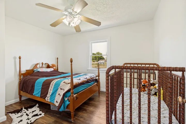 Bedroom featuring wood-finish flooring, a ceiling fan with integrated lighting, and white trim around the window