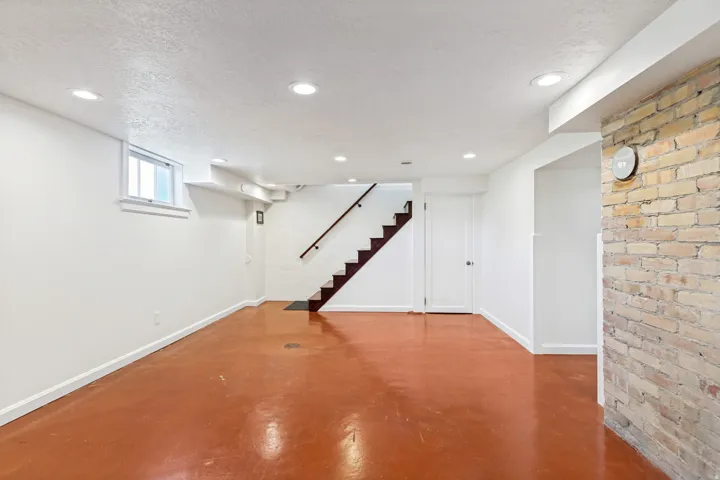 Lower level featuring a staircase with dark wood treads and a matching handrail, a partial exposed brick wall, white painted walls, a window, and recessed ceiling lighting