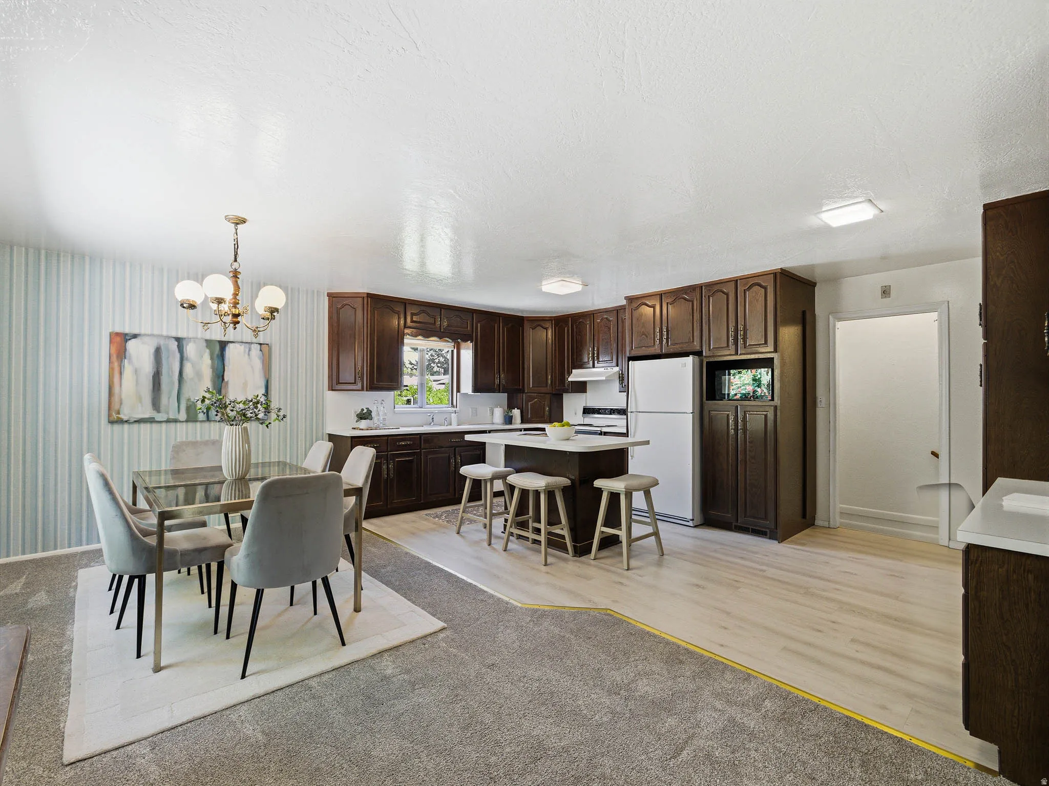 Open-concept kitchen and dining area featuring dark wood cabinetry, white countertops, and a central kitchen island with seating