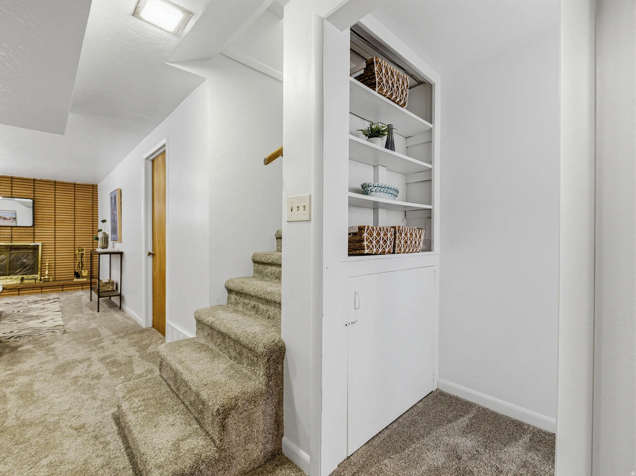 Carpeted staircase featuring a built-in shelving unit, a white painted handrail, and an overhead light fixture