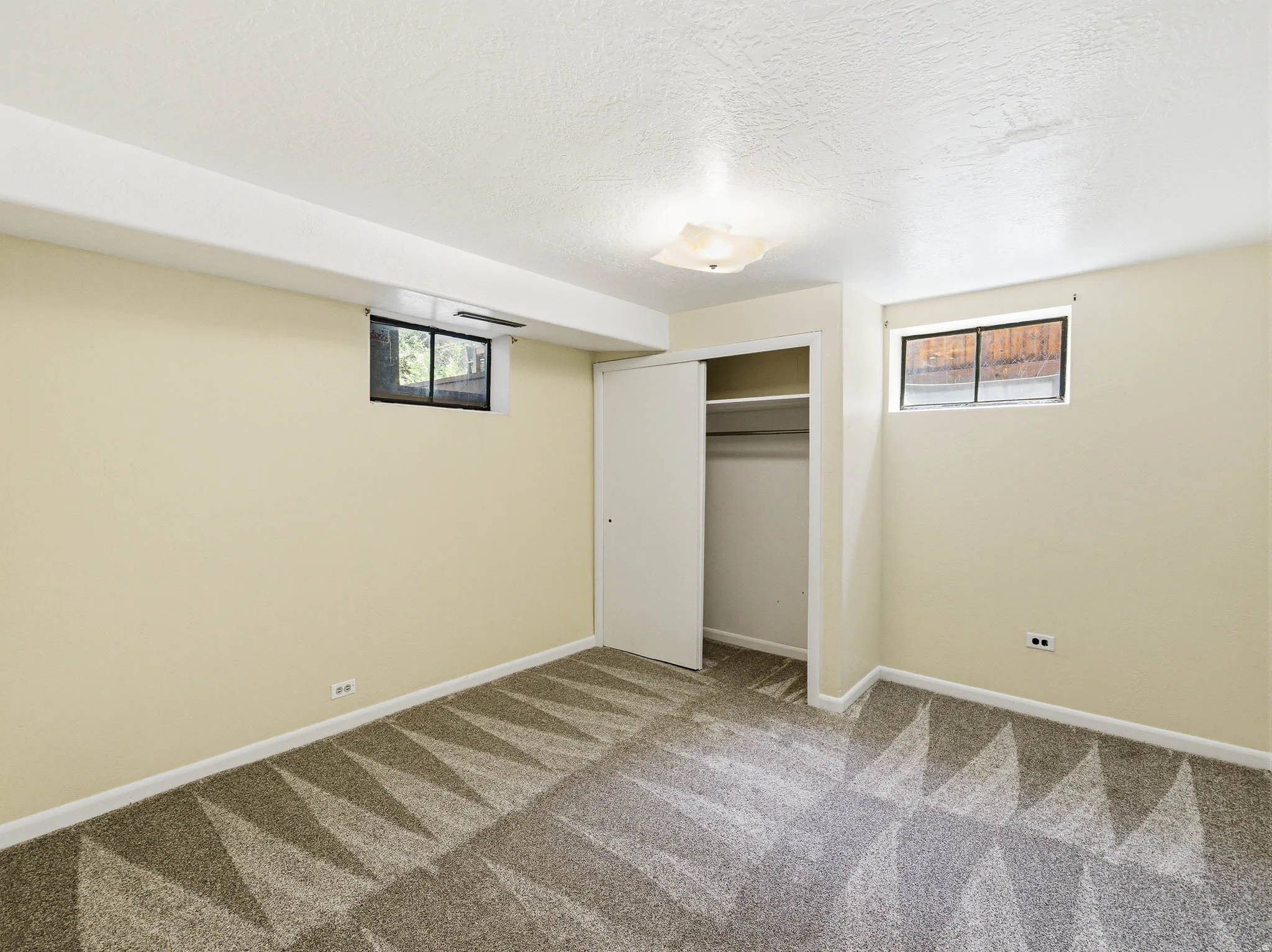 Room featuring patterned carpet flooring, light-toned wall paint, two windows, and a sliding closet