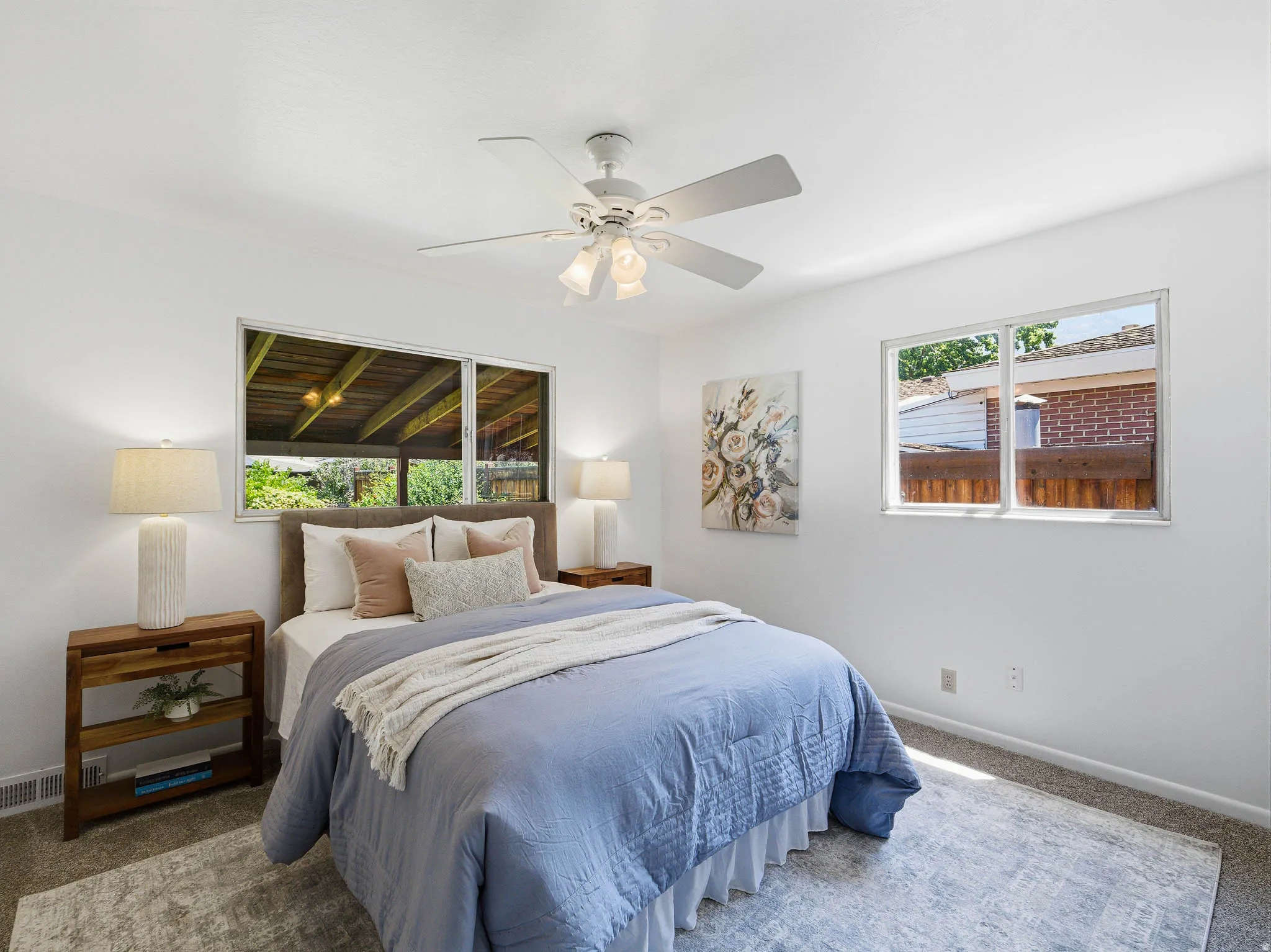 Bright bedroom featuring white walls, a ceiling fan with integrated lighting, and two windows providing natural illumination