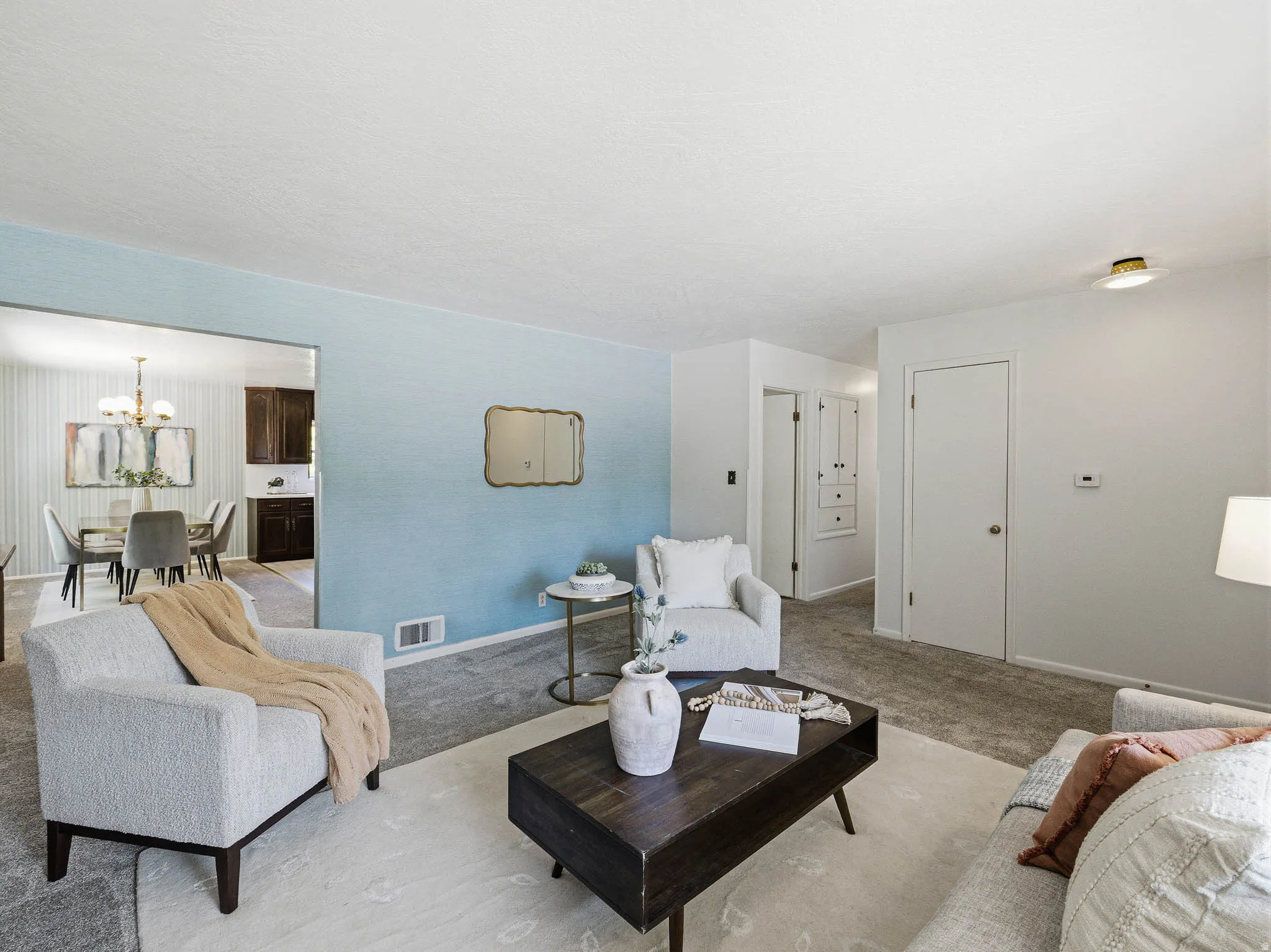 Living area featuring light gray carpet flooring, a light blue accent wall, and a recessed dining space with a chandelier