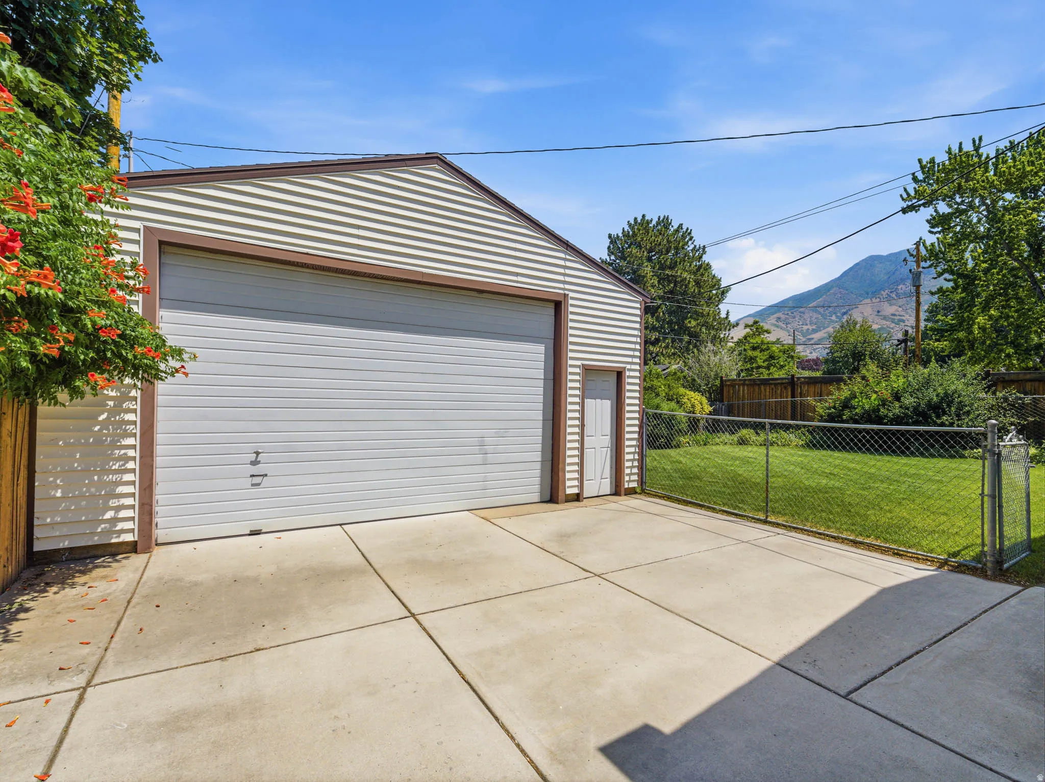 Detached two-car garage with an additional side entry door, concrete driveway, and a fenced backyard featuring a mountain backdrop