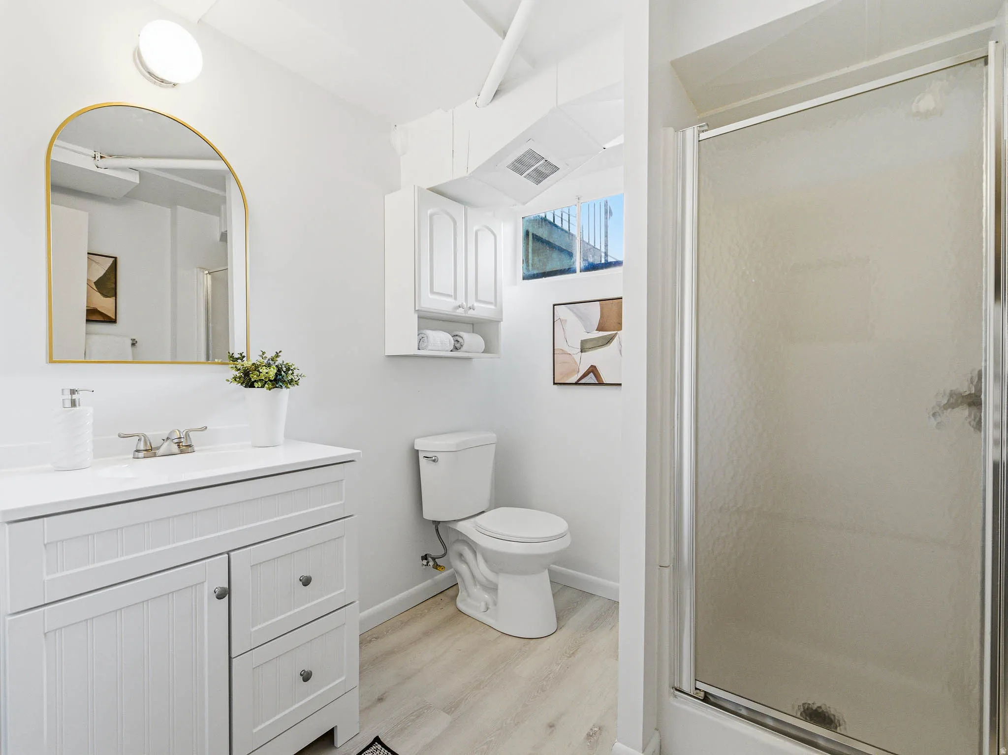 White vanity with a quartz countertop, brushed nickel faucet, and gold-framed arched mirror