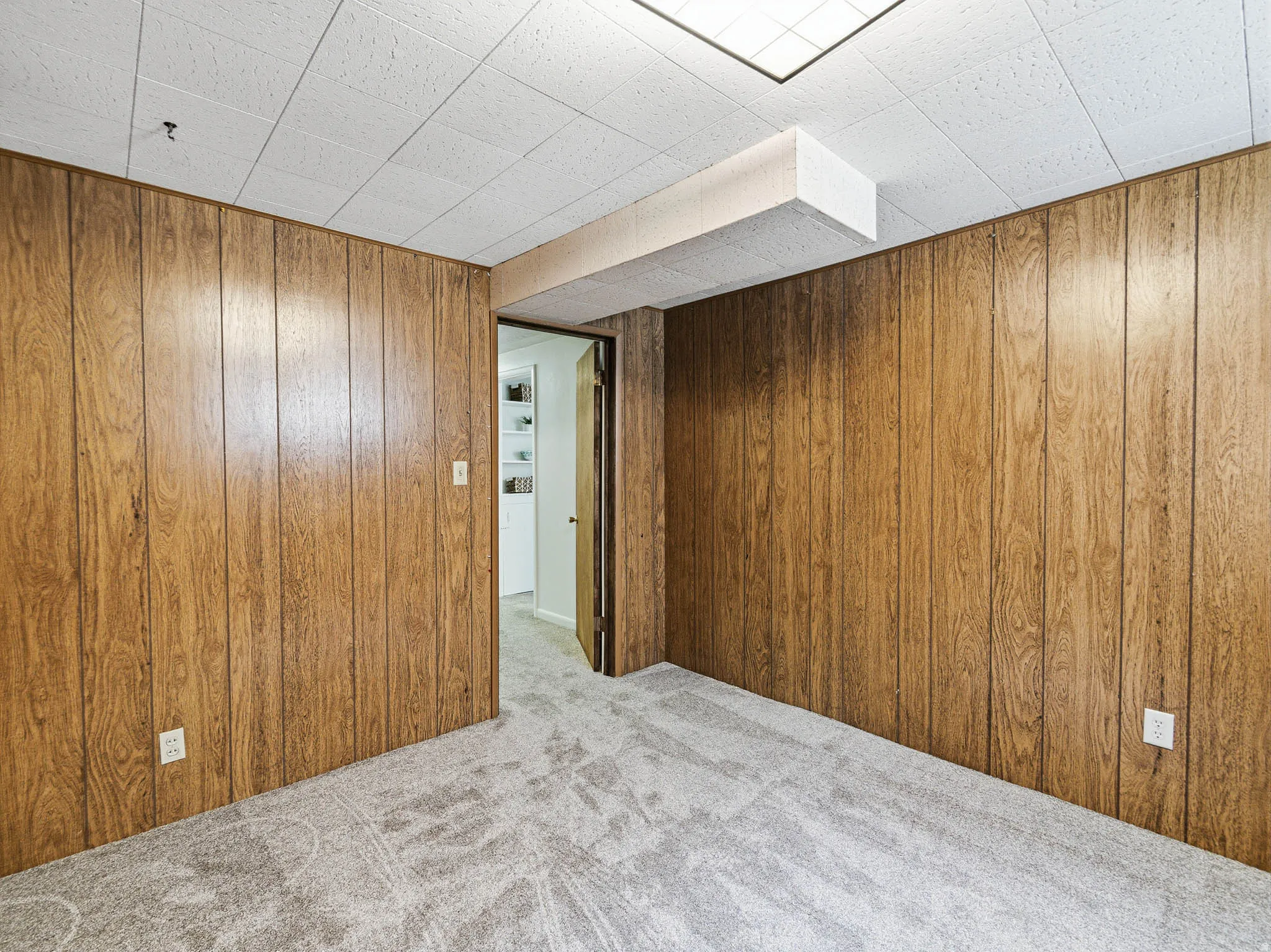 Room featuring wood paneling, grey patterned carpeting, and a drop ceiling with recessed lighting