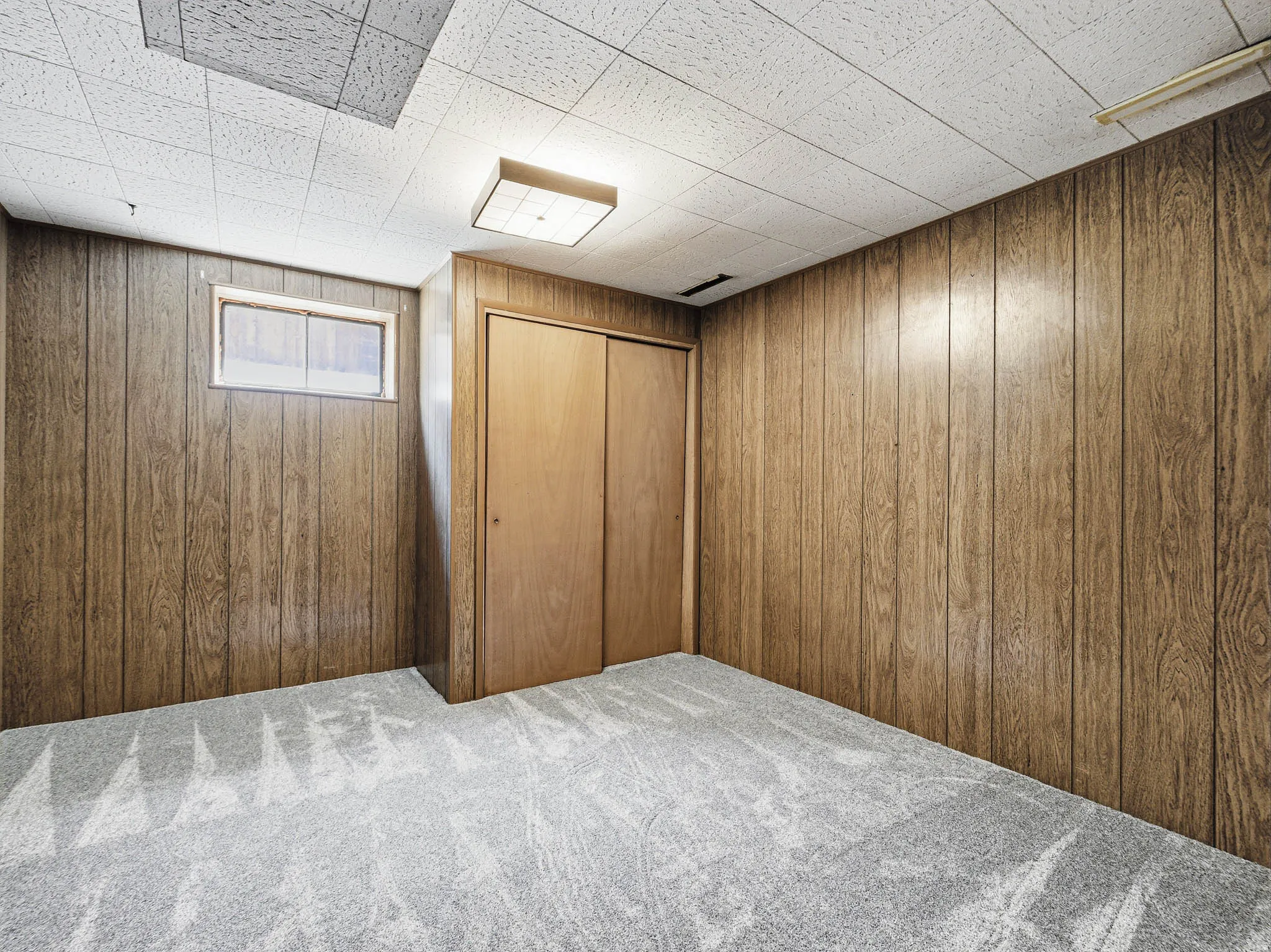 Room featuring wood-finish paneling, light gray patterned carpet, and a drop ceiling
