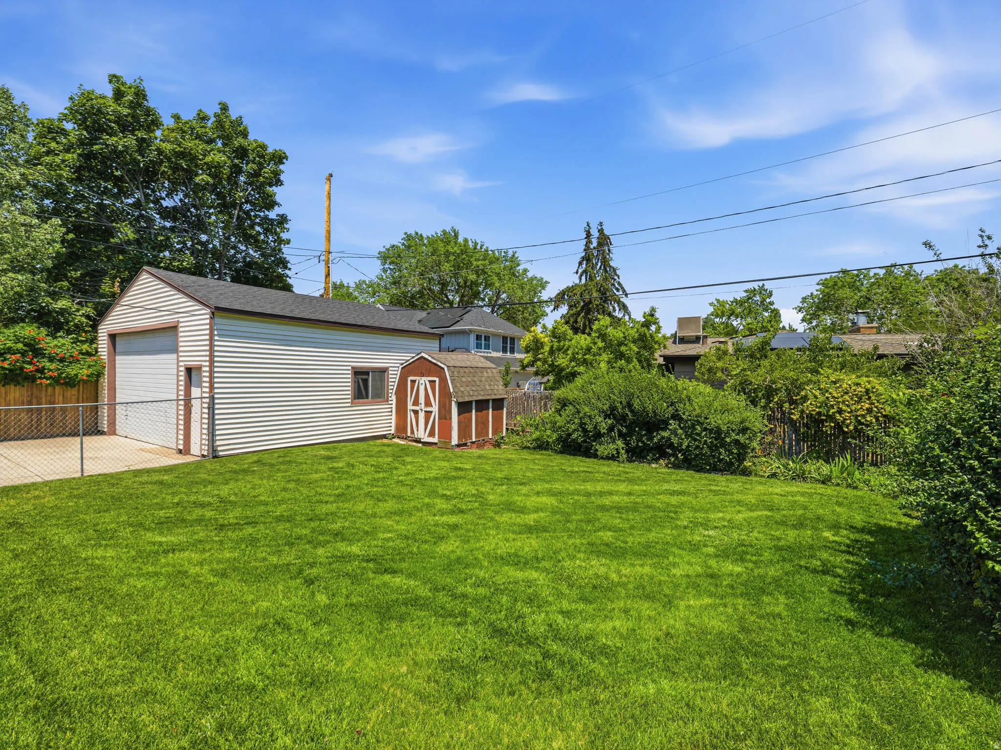 Expansive green lawn featuring a detached garage with a roll-up door, a red barn-style shed, and a chain-link fence