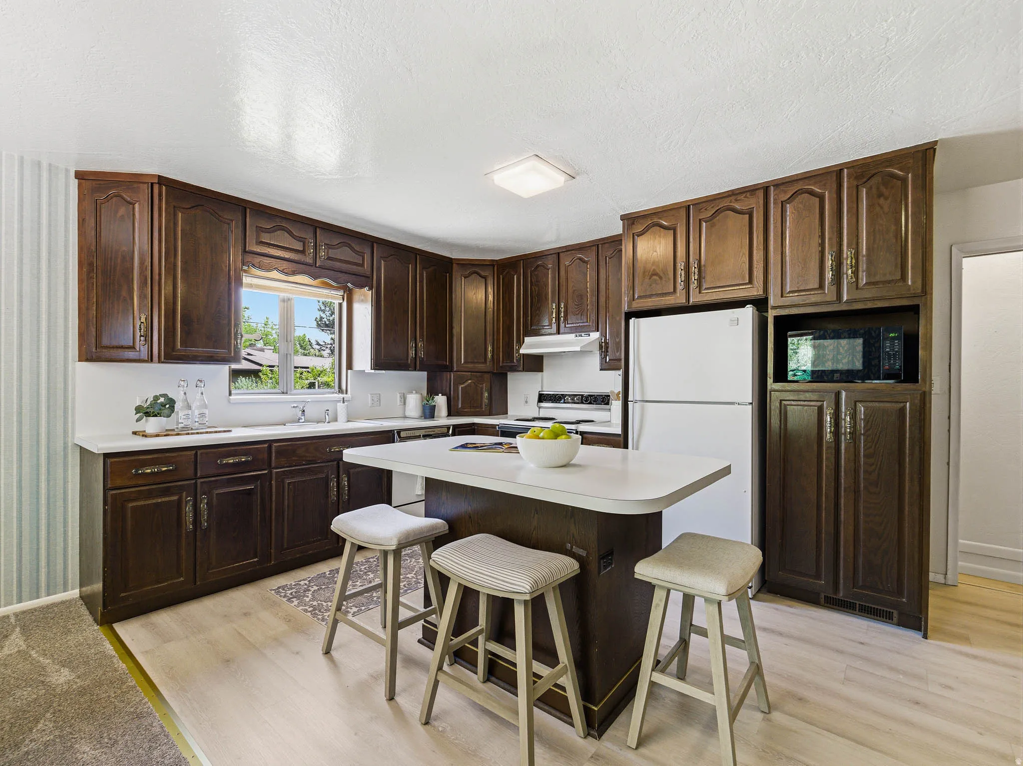 Kitchen featuring extensive wood cabinetry, light countertops, wood-finish flooring, and a built-in kitchen island with seating