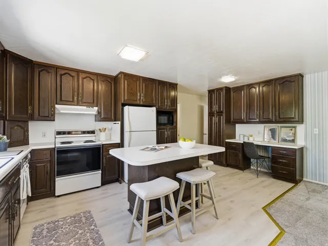 Kitchen featuring wood cabinetry, white countertops, a central island with seating, a built-in desk area, and wood-finish flooring