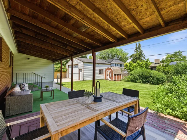 Covered patio with exposed wood ceiling beams, featuring a wood-finish deck and a green turf area