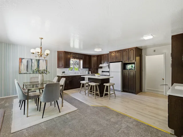Open-concept kitchen and dining area featuring dark wood cabinetry, white countertops, and a central kitchen island with seating