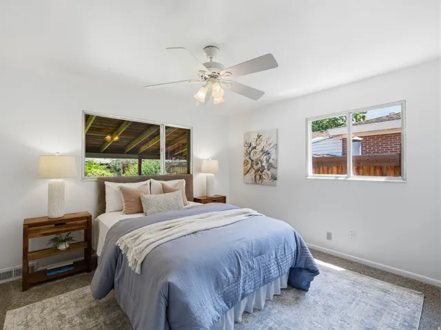 Bright bedroom featuring white walls, a ceiling fan with integrated lighting, and two windows providing natural illumination