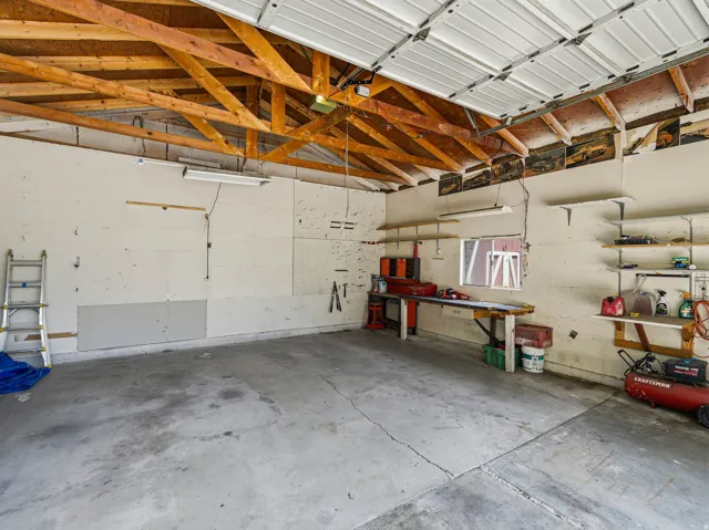 Attached garage interior featuring exposed wood ceiling trusses and a concrete floor