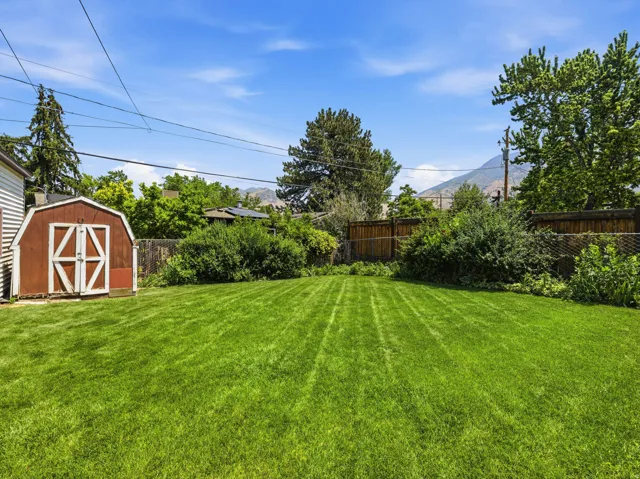Expansive green lawn with a storage shed featuring white trim