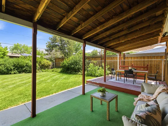 Covered patio area featuring a stained wood ceiling and support beams, a red-stained wood deck, and a green artificial turf floor