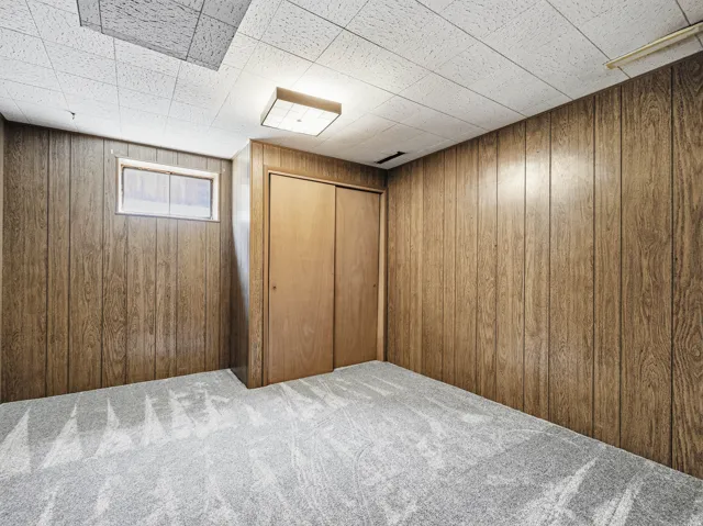 Room featuring wood-finish paneling, light gray patterned carpet, and a drop ceiling