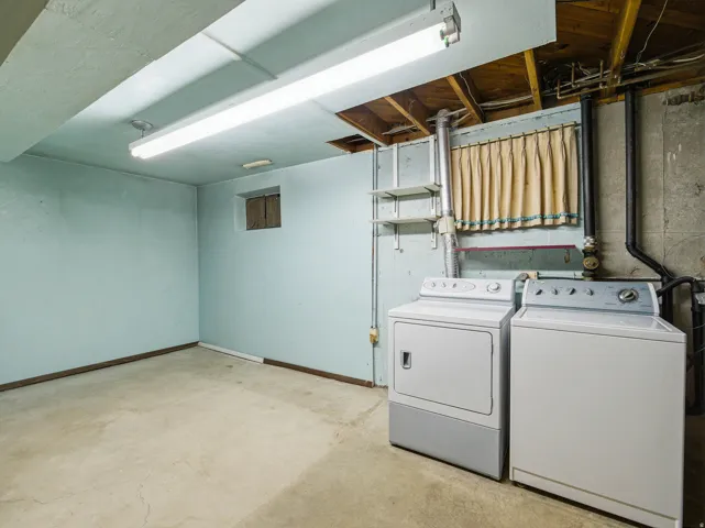 Utility room featuring a concrete floor, light blue painted walls, exposed ceiling joists, and a small built-in window