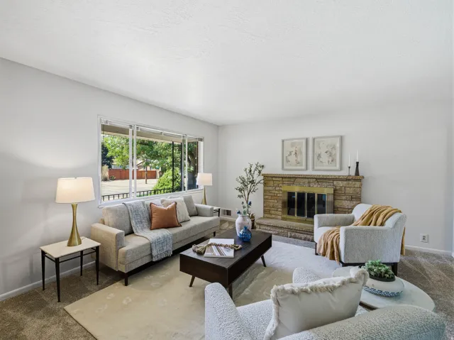 Living area featuring a stone-clad fireplace with a brass firebox, large picture window, and neutral wall color