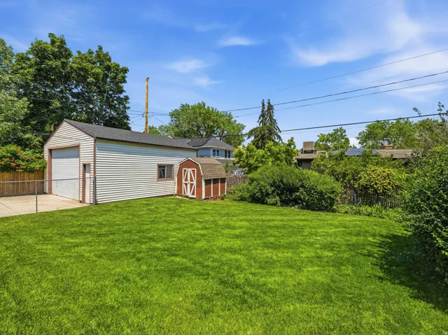 Expansive green lawn featuring a detached garage with a roll-up door, a red barn-style shed, and a chain-link fence