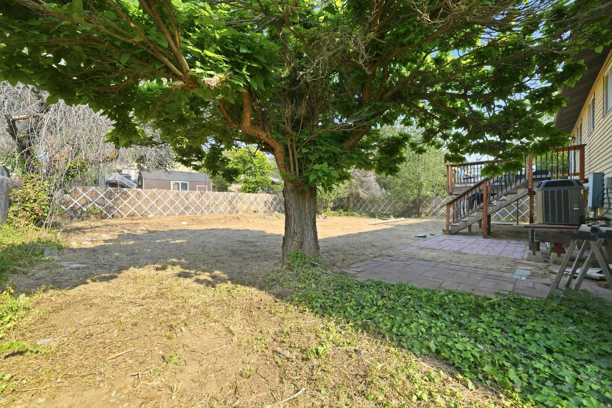 Backyard featuring a mature tree, stone patio, and wood deck with railings