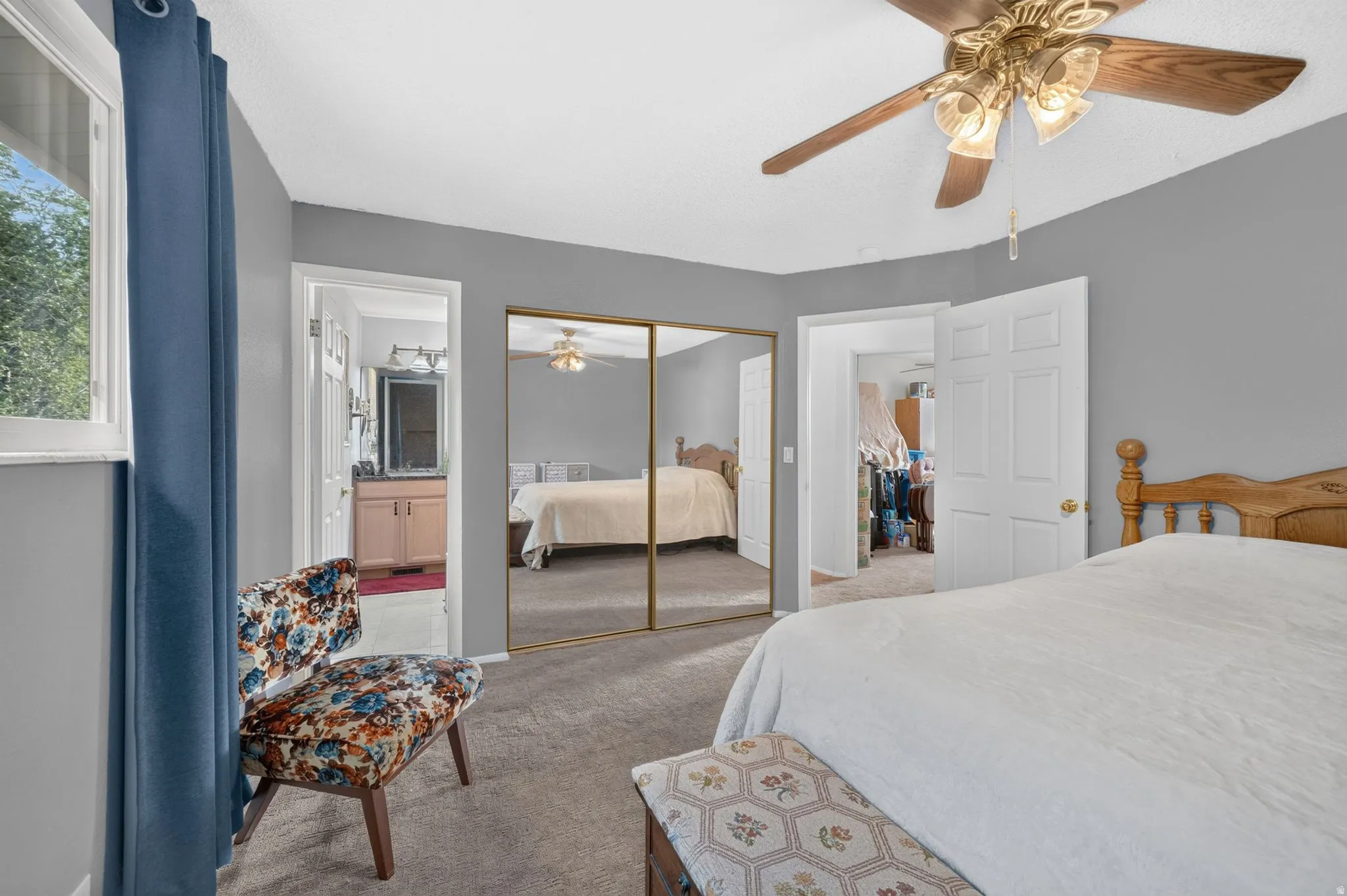 Carpeted MASTER bedroom featuring a ceiling fan with integrated lighting, a window with a blue curtain, and mirrored wardrobe doors