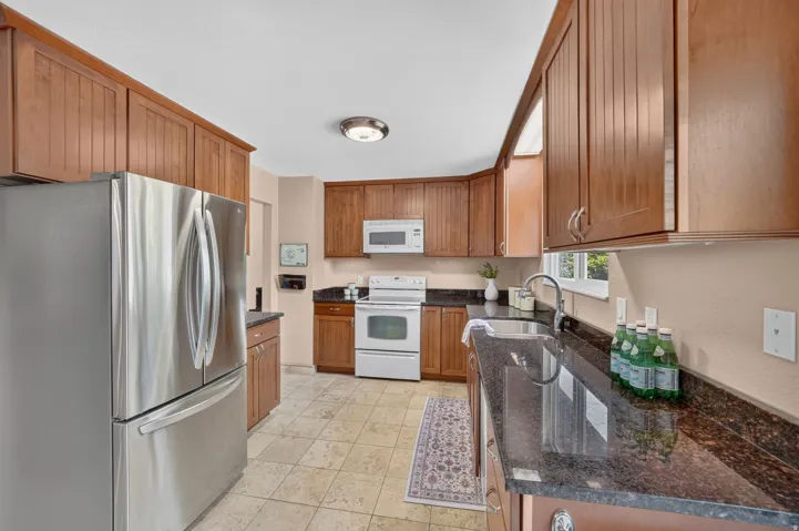 Kitchen featuring extensive wood cabinetry, dark countertops, tiled flooring, and a stainless steel refrigerator