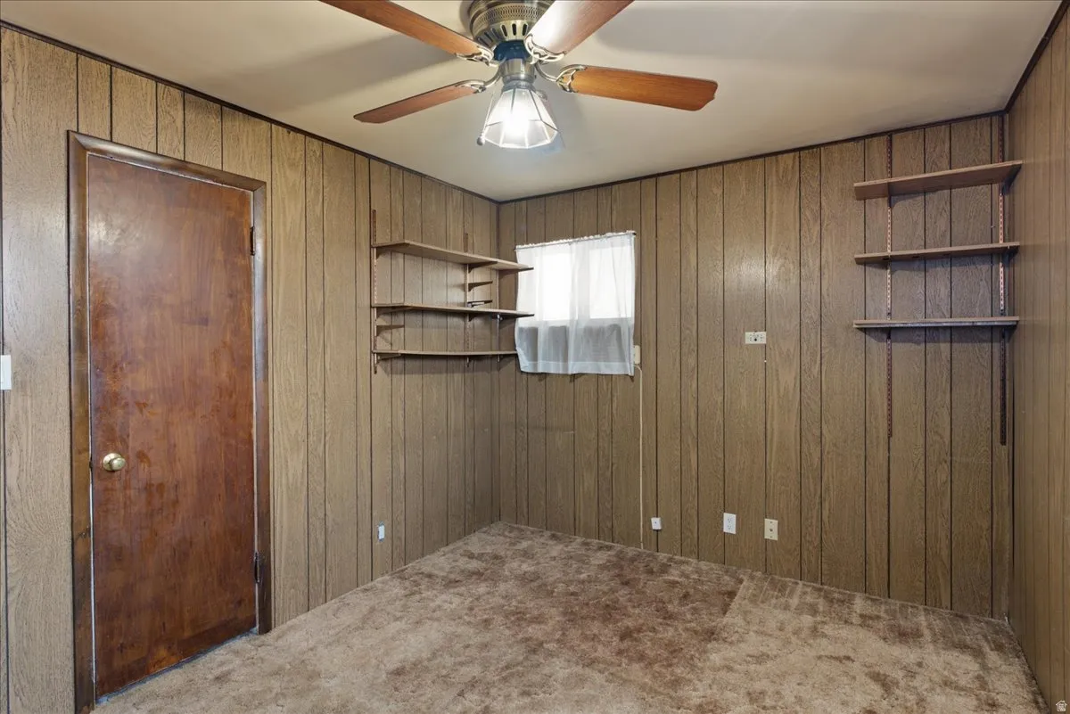 Room featuring wood paneling, a ceiling fan with light fixture, and brown carpeting