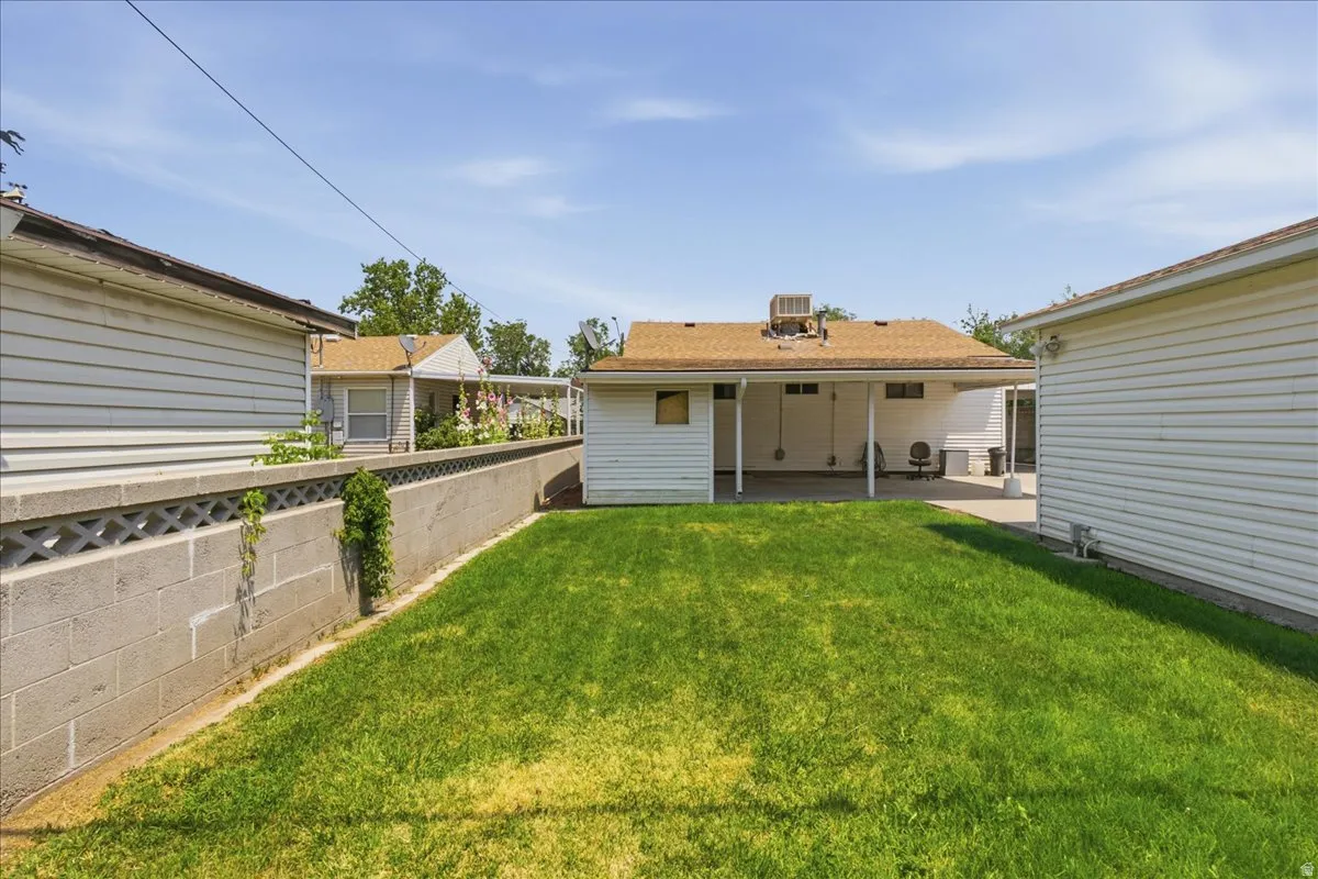 Expansive backyard featuring a manicured lawn, concrete block retaining wall, and a covered concrete patio