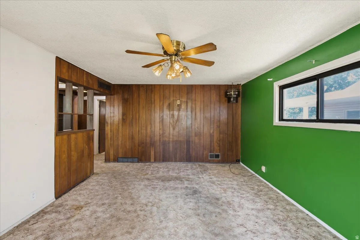 Living area featuring wood paneling, a ceiling fan with integrated lighting, and a single window with black framing