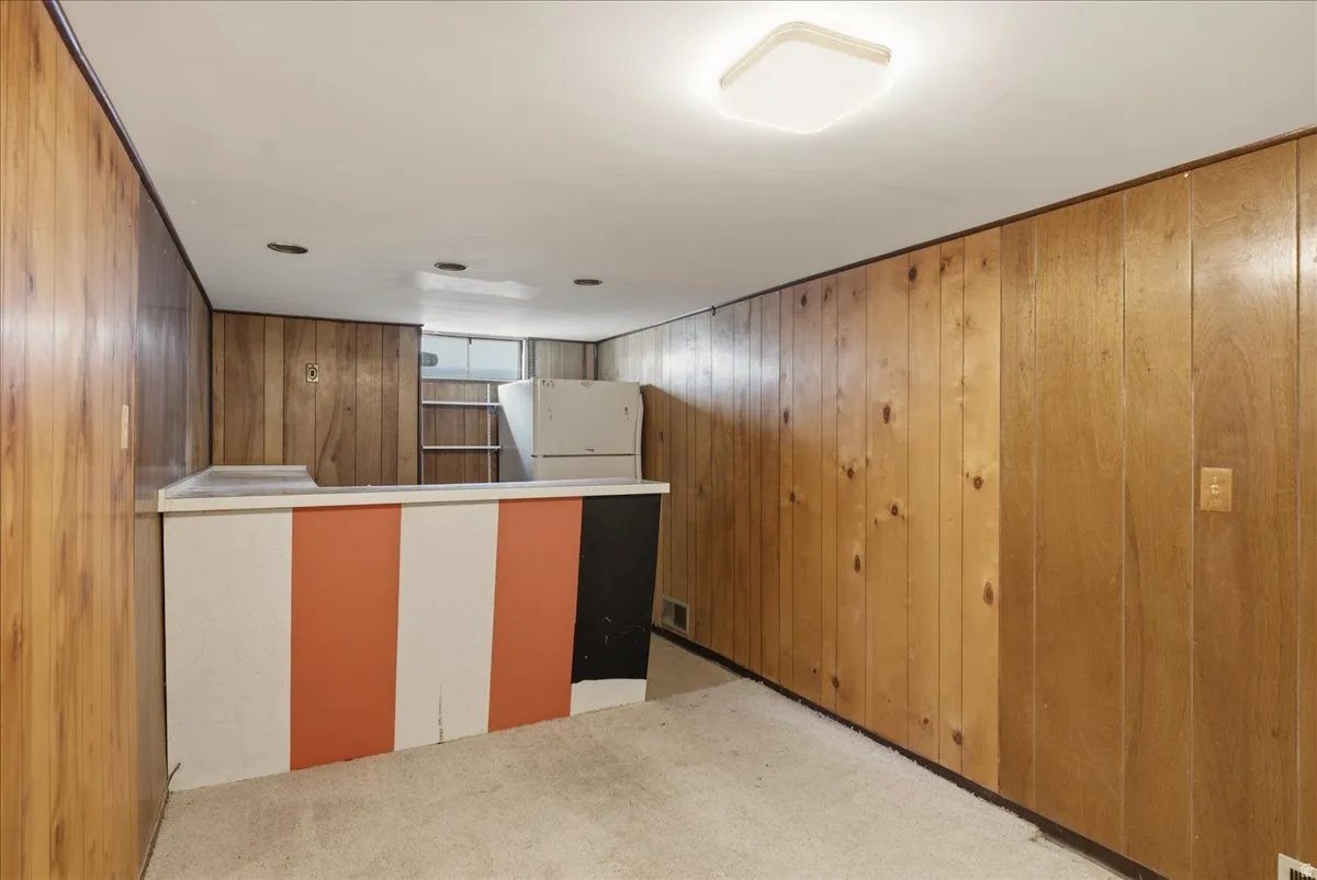Recreation room featuring wood paneling, a built-in bar with a countertop, carpeted flooring, and a flush-mount ceiling light fixture