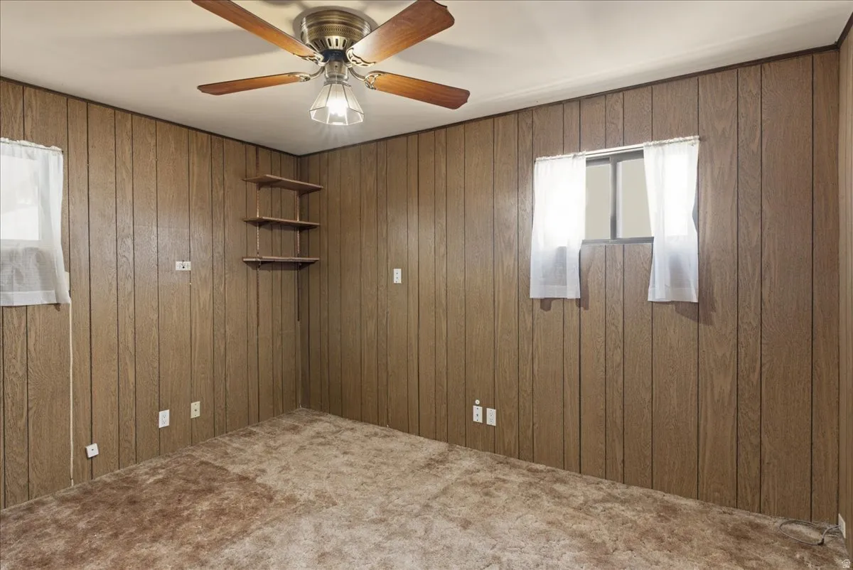Room featuring wood-paneled walls, carpeted flooring, and a ceiling fan with integrated lighting